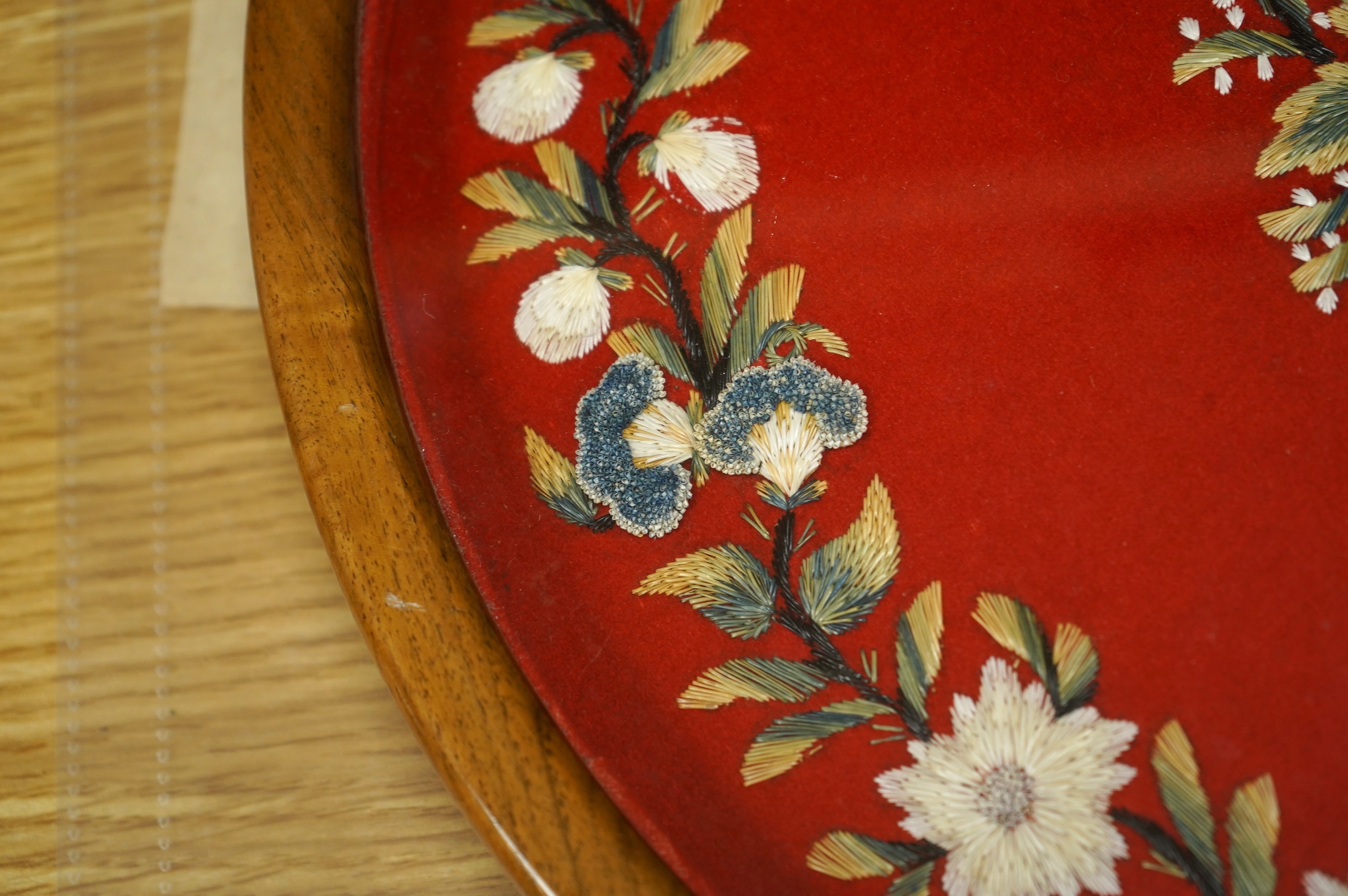 A framed, 19th century, possibly Scandinavian, red felt circular multi-coloured silk embroidery of flowers, acorns and leaves, also embroidered with fine stump work style beadwork flower detail, 32cm diameter. Condition